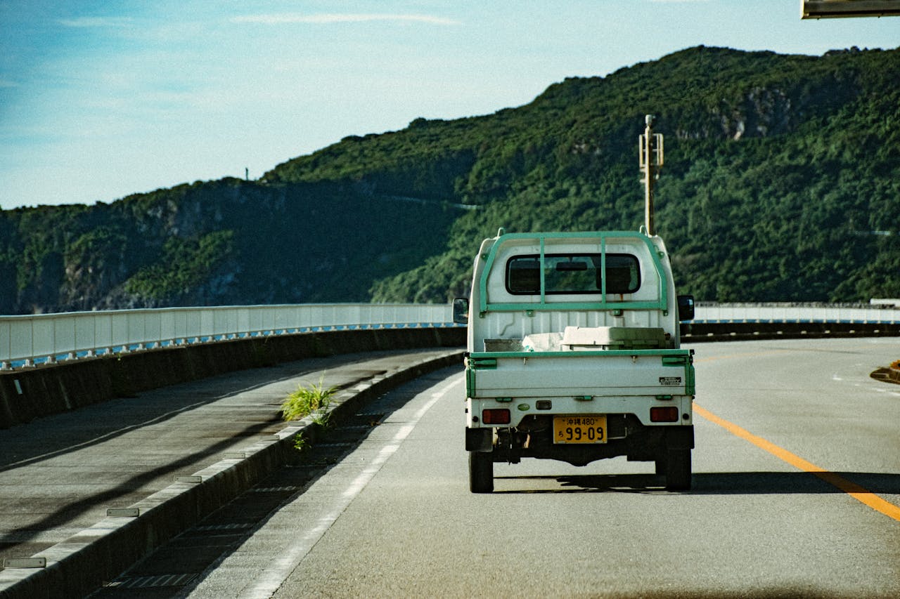 A pickup truck on a scenic road in Okinawa, Japan, surrounded by lush greenery.