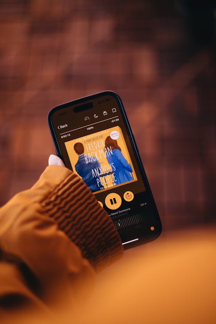 Close-up of a person holding a smartphone displaying an audiobook app.